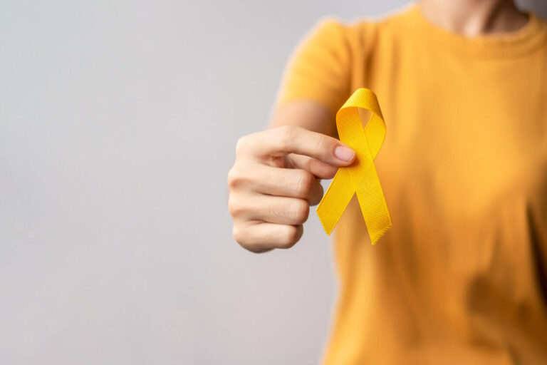 Pessoa vestindo camiseta amarela segurando um laço amarelo, símbolo da campanha Julho Amarelo de prevenção e conscientização sobre hepatite e cuidados com o fígado, destacando a importância das vitaminas para o fígado.